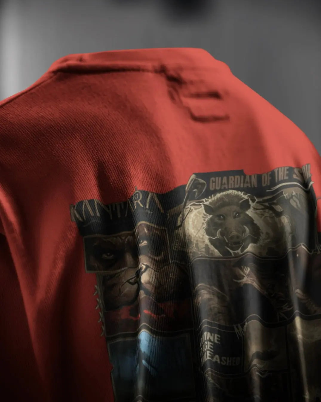 “Detailed shot of the graphic print on the back of a red Kantara-themed t-shirt, featuring a wild boar and character artwork with the text ‘Guardian of the Soil’.”