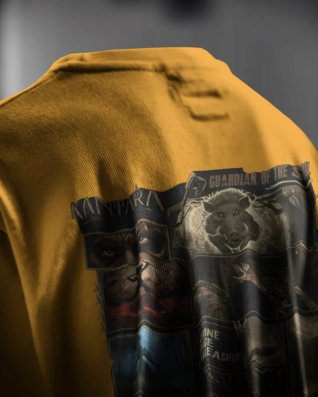 “Detailed shot of the graphic print on the back of a yellow Kantara-themed t-shirt, featuring a wild boar and character artwork with the text ‘Guardian of the Soil’.”